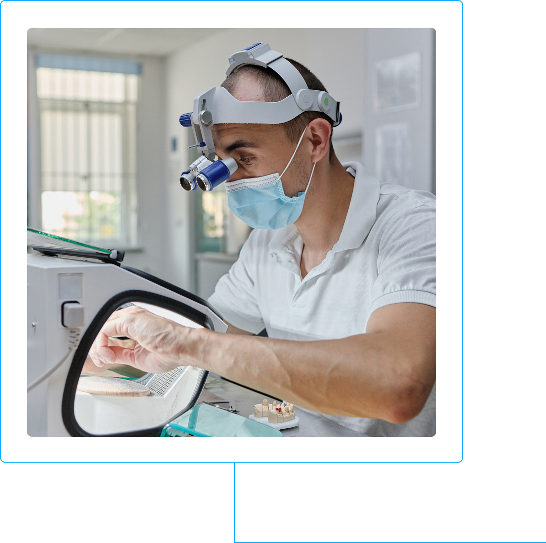 Denturologiste concentre, loupe binoculaire et masque, travaillant sur une prothese dentaire, illustrant une carriere stimulante en denturologie au Quebec.