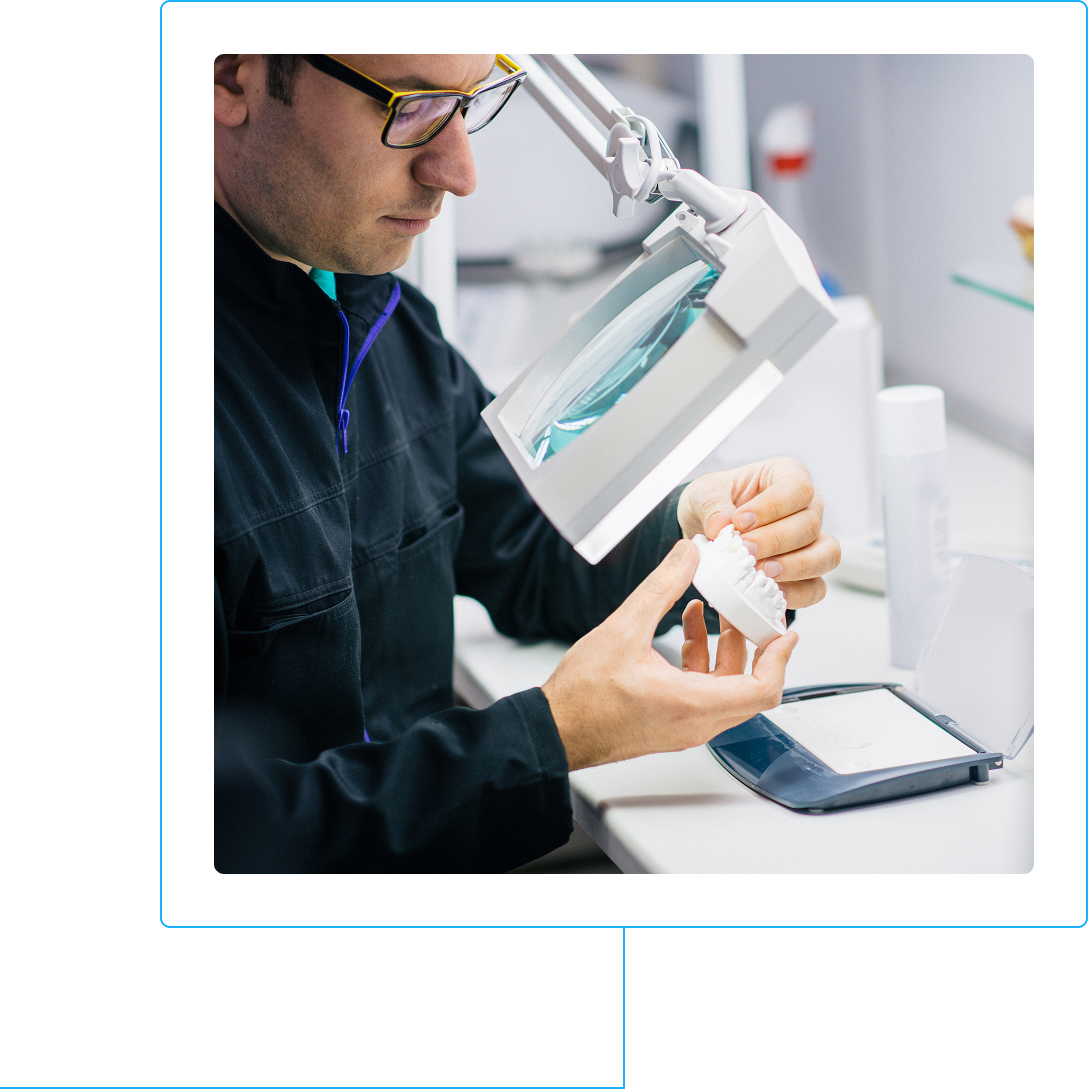 Denturologiste au travail en laboratoire, examinant une prothese dentaire, illustrant son role essentiel dans la fabrication de protheses au Quebec.
