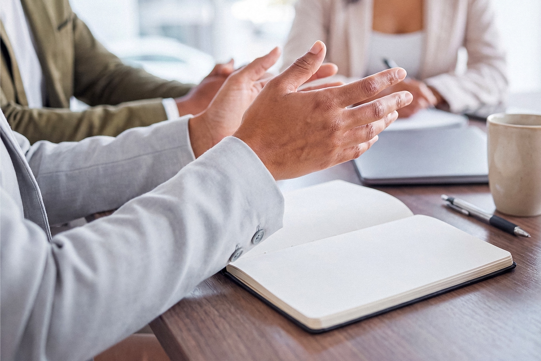 Gros plan sur des mains gesticulant lors d'une rencontre de conseil, carnet ouvert, illustrant une démarche d'accompagnement en adoption au Québec.