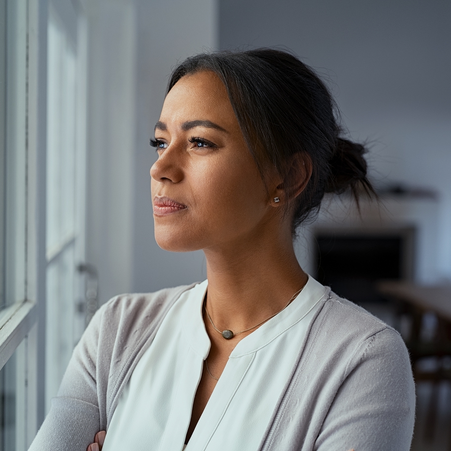 Une femme pensive regarde par la fenêtre, bras croisés, illustrant la réflexion d'une personne engagée dans une démarche d'adoption solo au Québec.