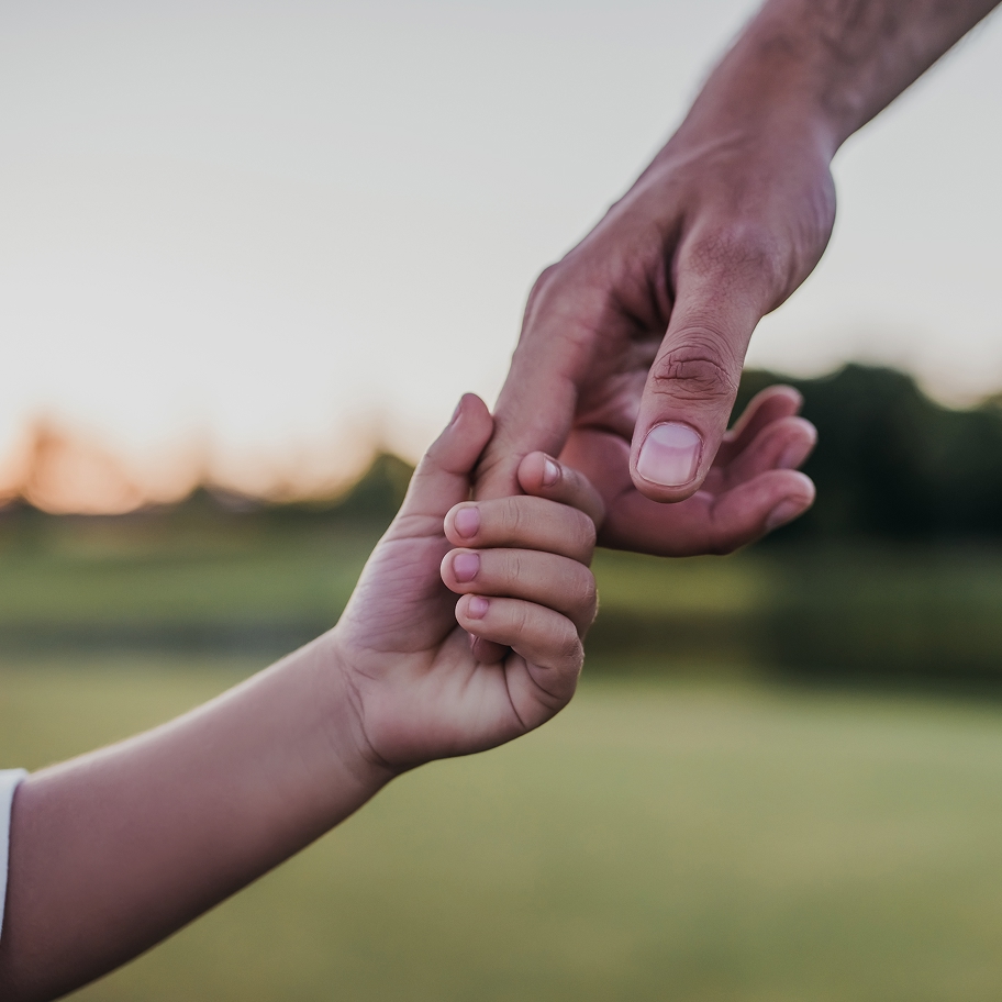 Gros plan sur la main d'un adulte tenant celle d'un enfant en plein air, symbolisant le lien créé lors d'une adoption via la banque mixte au Québec.